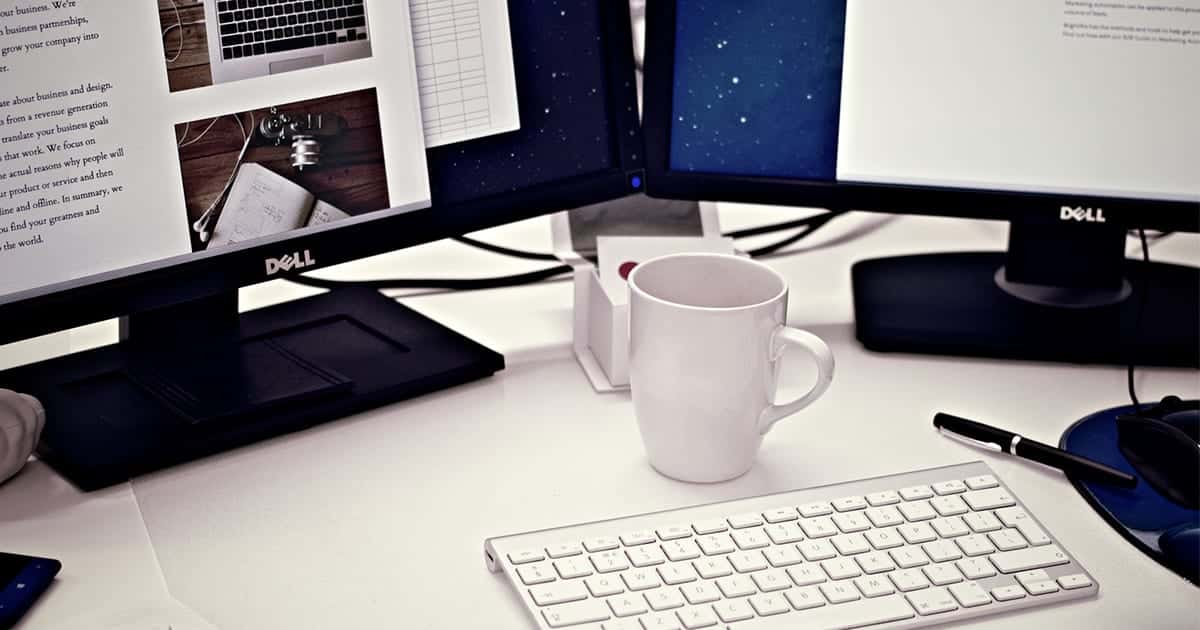 Desk with keyboard, white coffee cup and computer monitors.