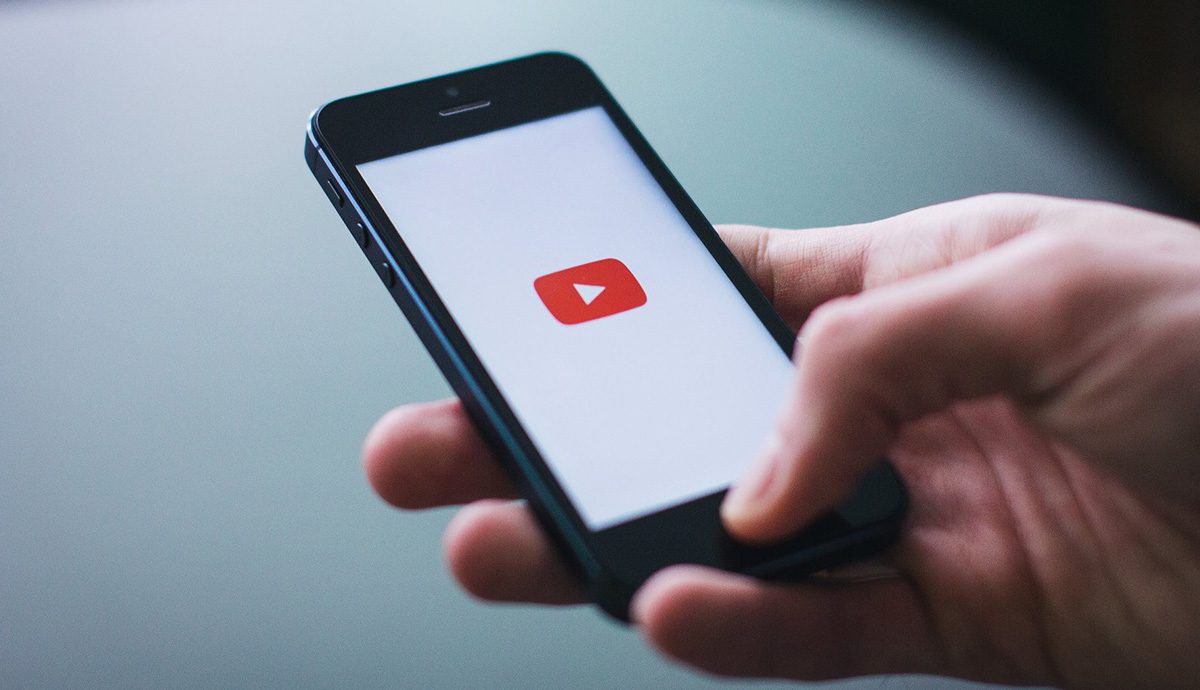 Hand holding phone with YouTube icon on screen.