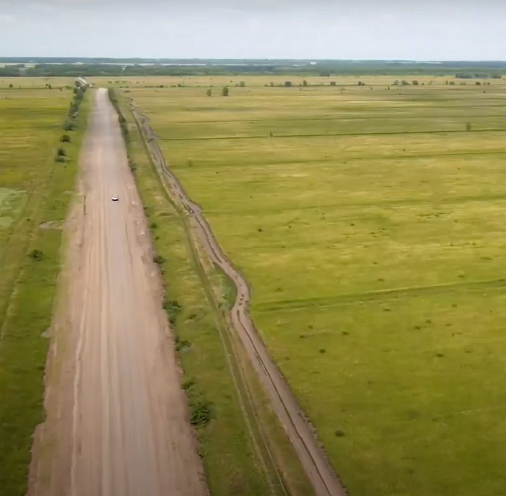 Aerial shot of a rural dirt road that runs through open grassland.