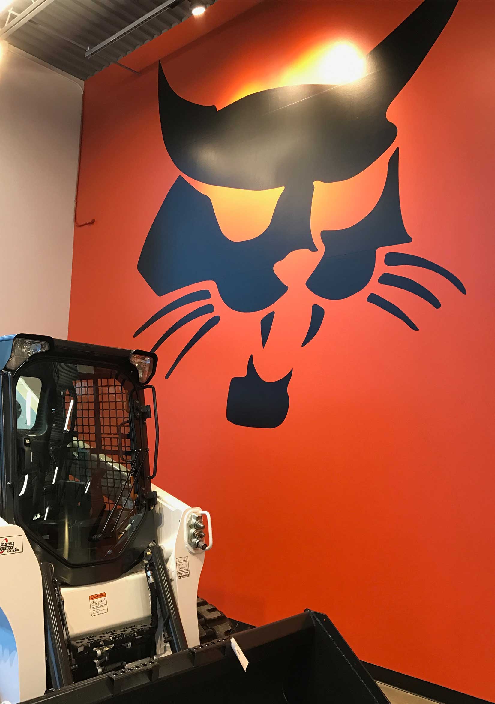 A large, black, vinyl sign of Bobcat’s logo on an orange wall