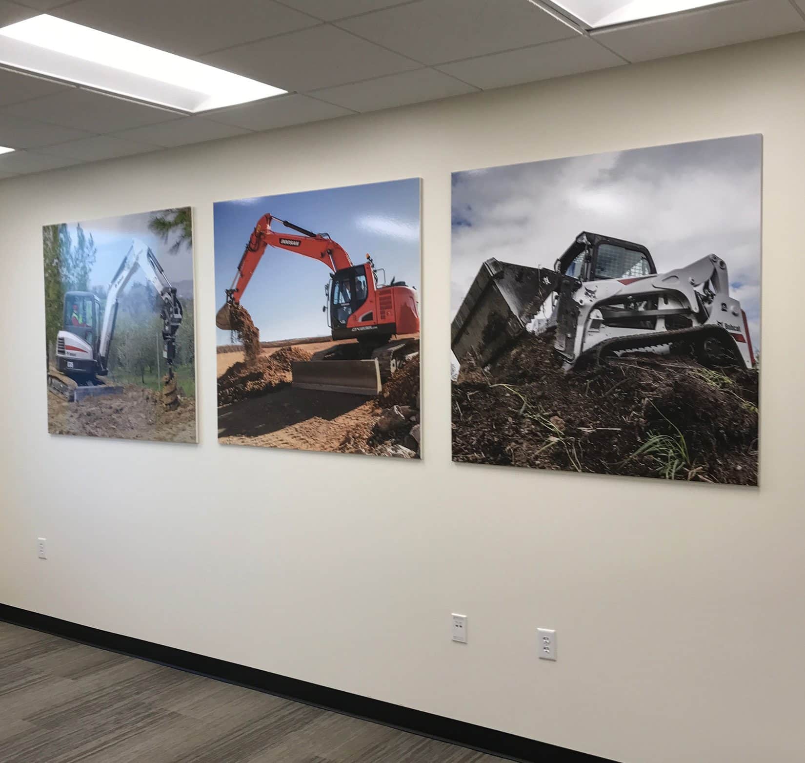 Three signs displaying photos of Bobcat machinery on a white wall