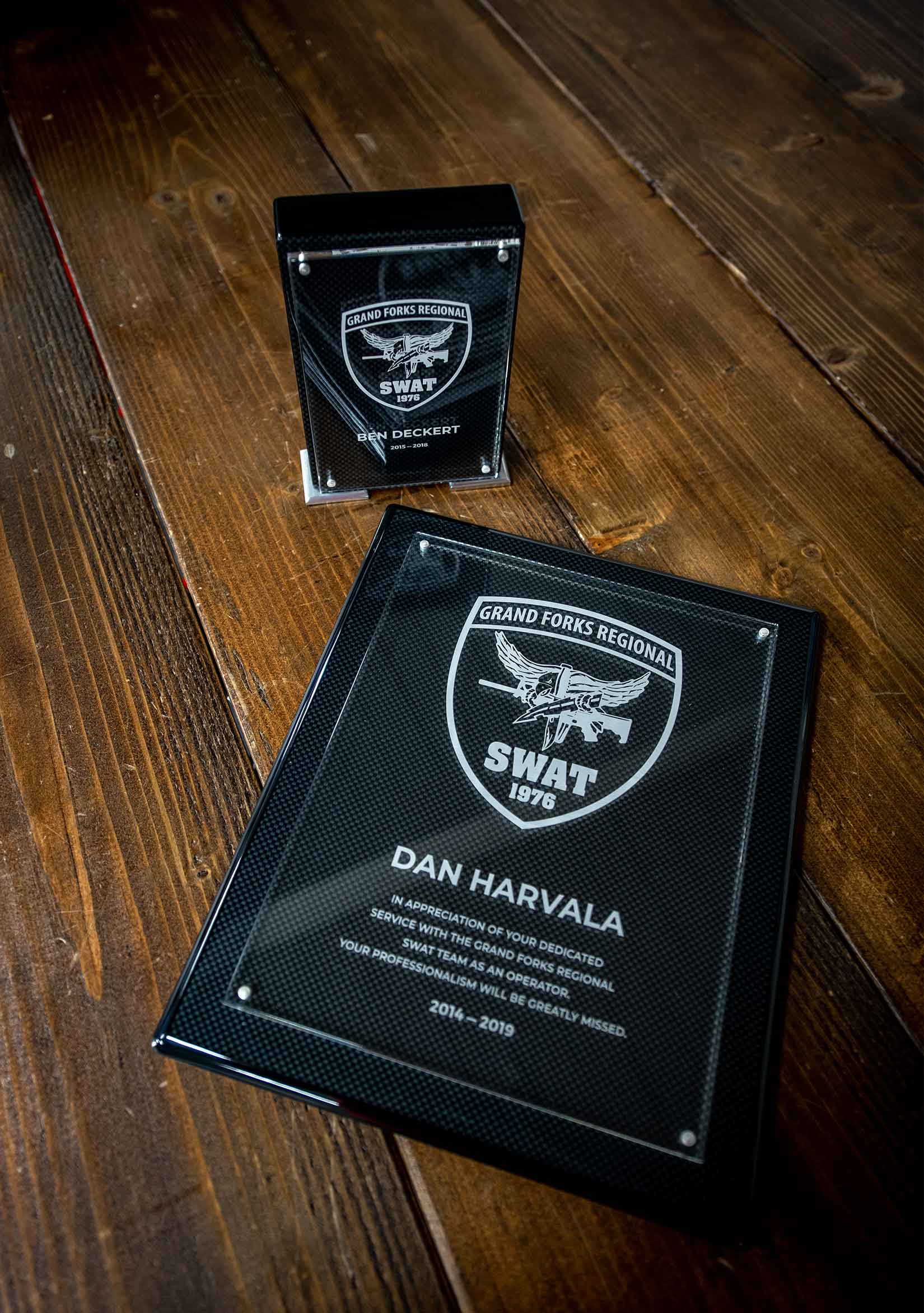 Two black carbon fiber plaques on a wooden table