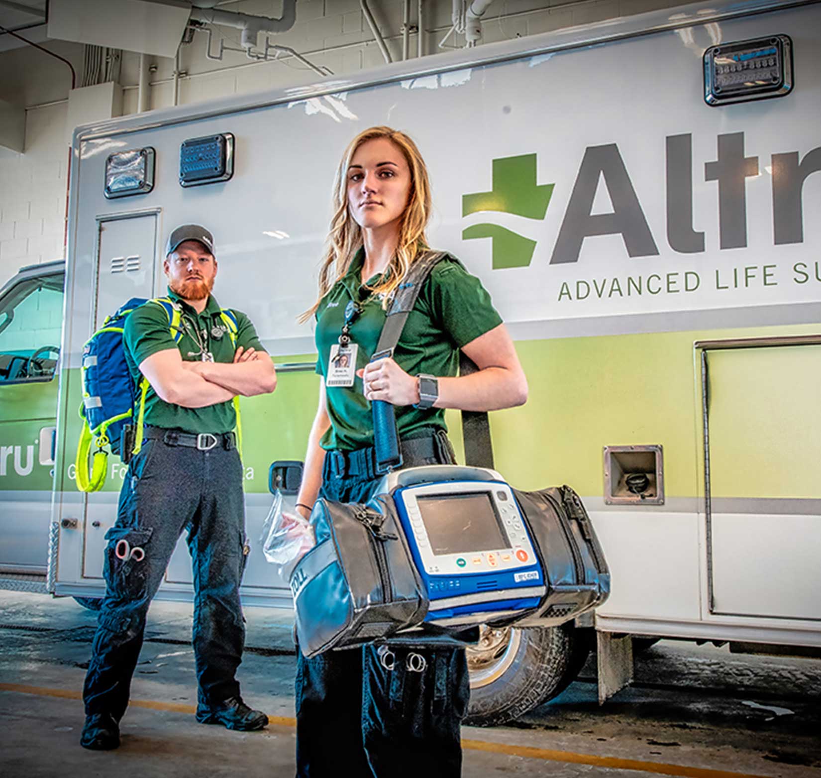 A professional photo of two Altru Hospital emergency medical technicians standing in front of an ambulance