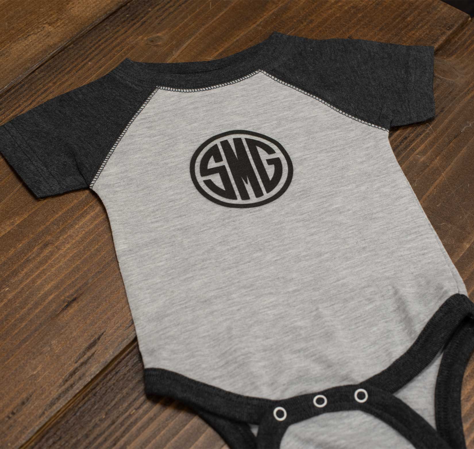A gray and white baby onesie screen printed with a black Stray Media Group logo