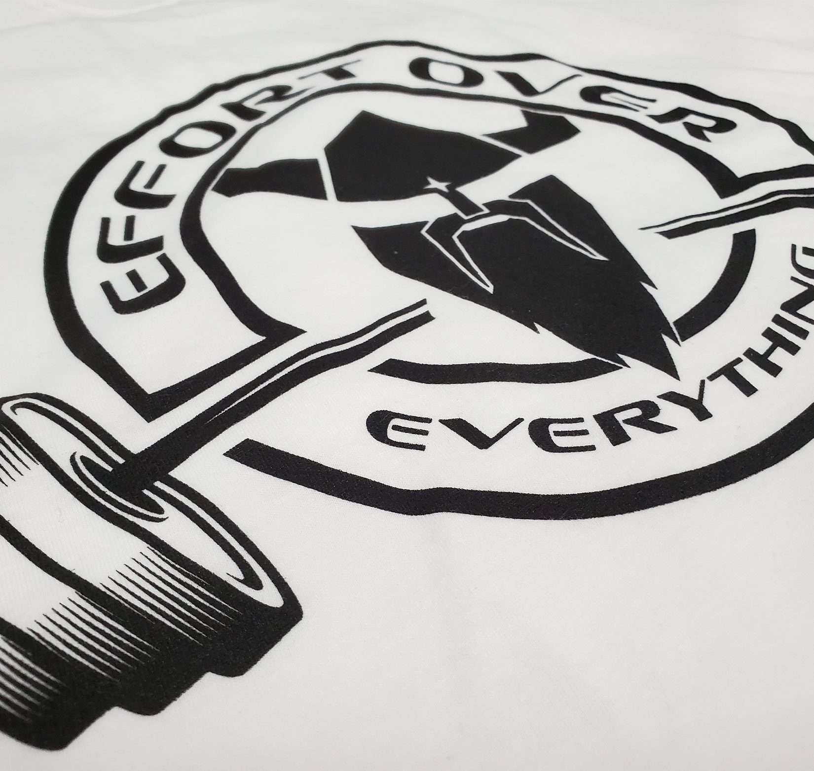 A closeup of a black “effort over everything” logo screen printed on a white shirt