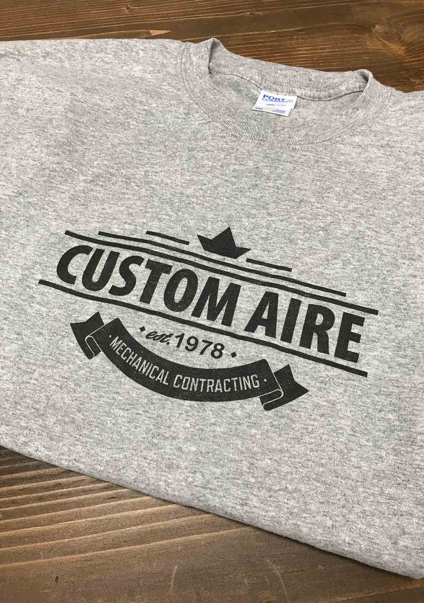 A light gray t-shirt screen printed with a Custom Aire logo in the center of the shirt