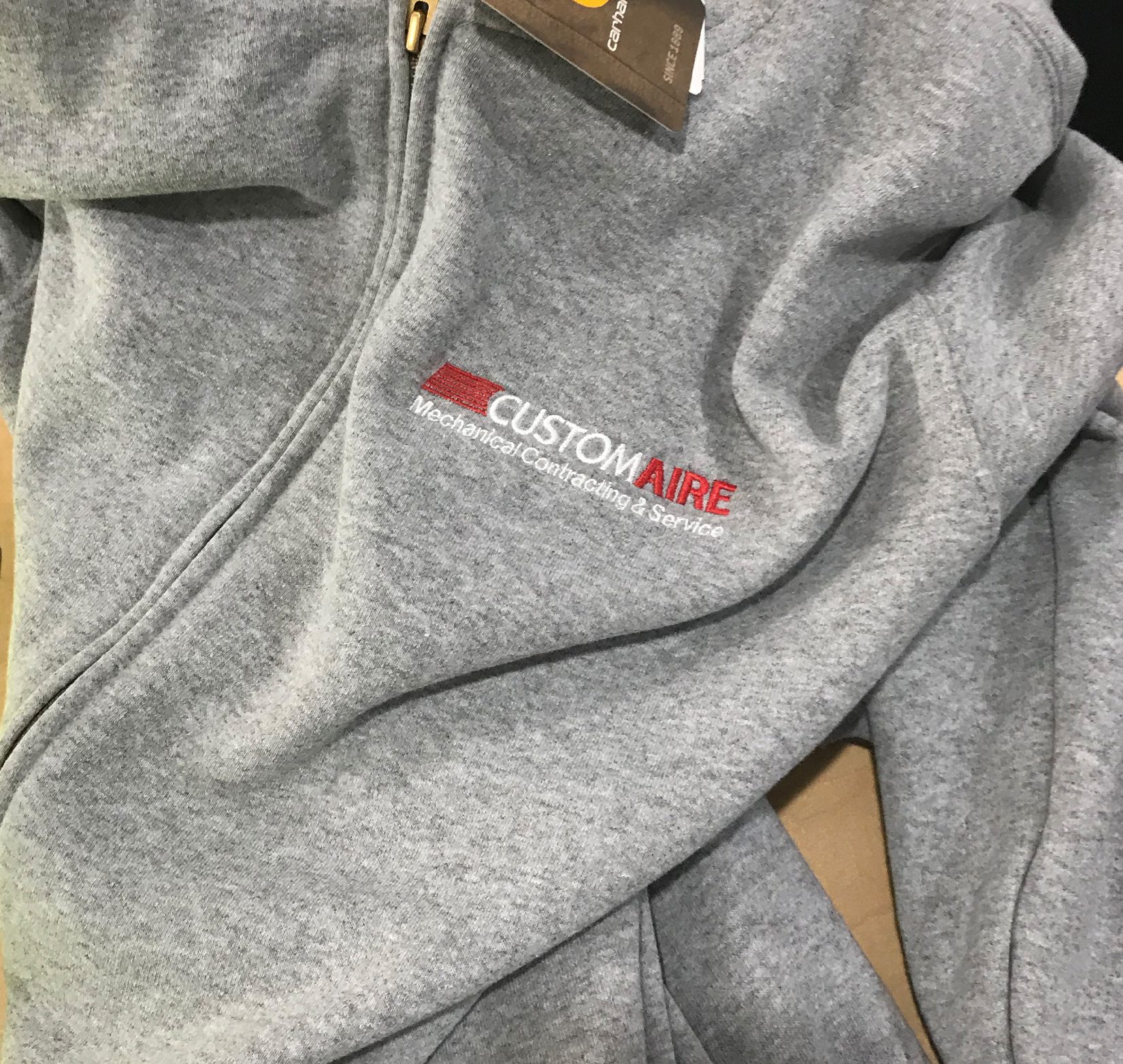 A close up of a white and red Custom Aire logo embroidered on a gray hoodie