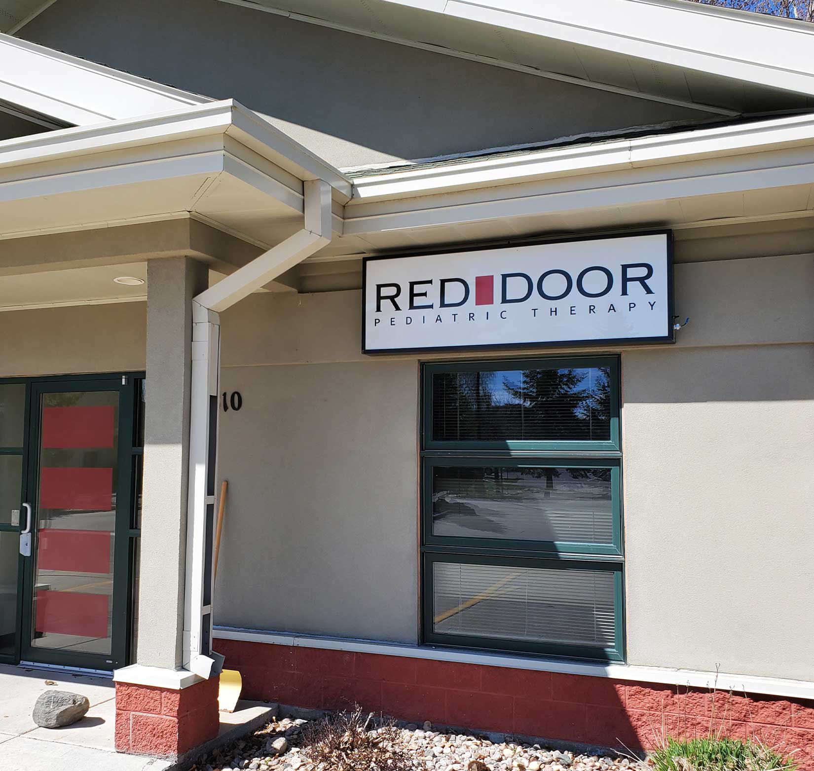 A company sign for Red Door Pediatric Therapy hanging in the front of its building