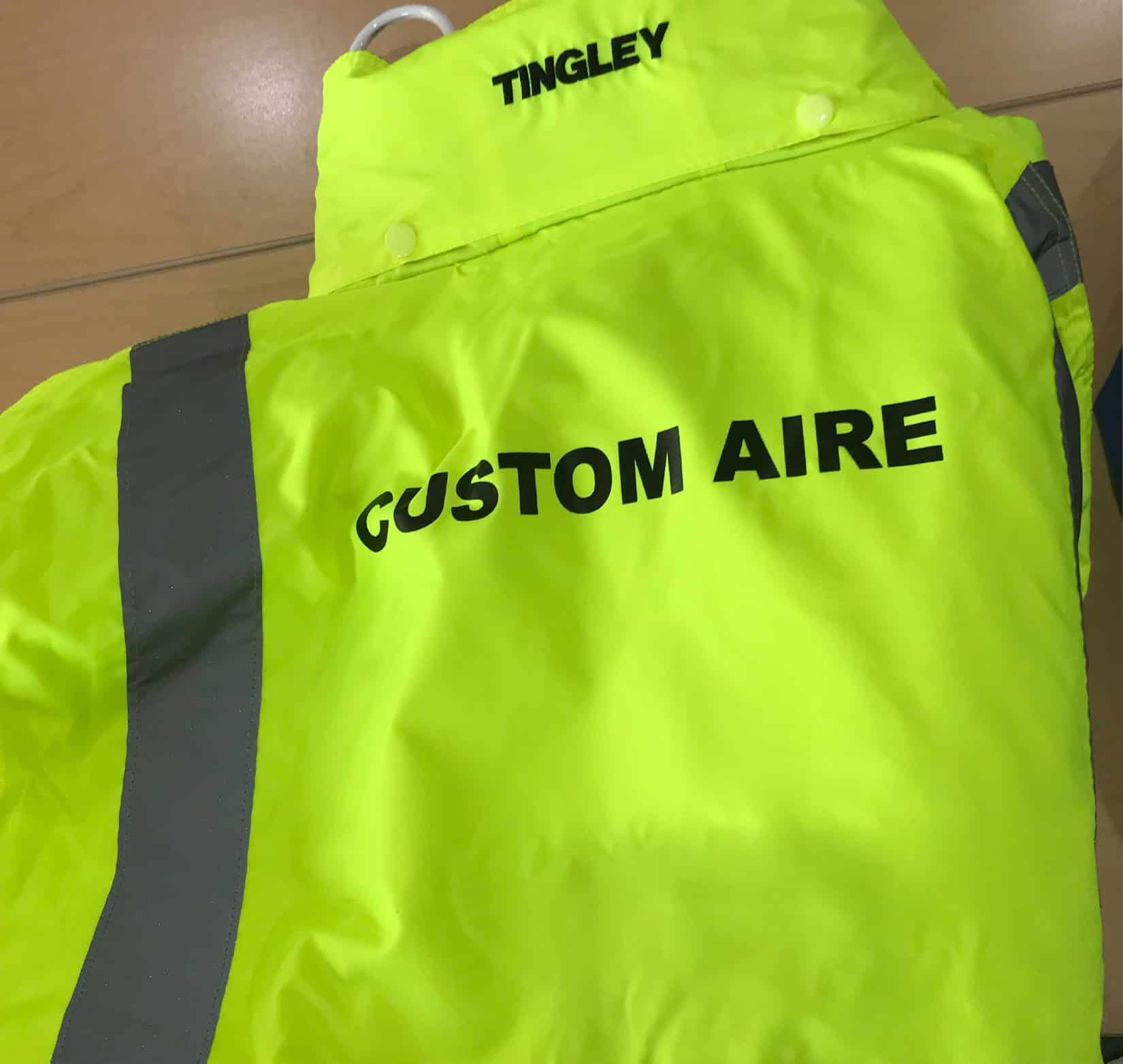 “Custom Aire” screen printed in black on the back of a neon green safety vest
