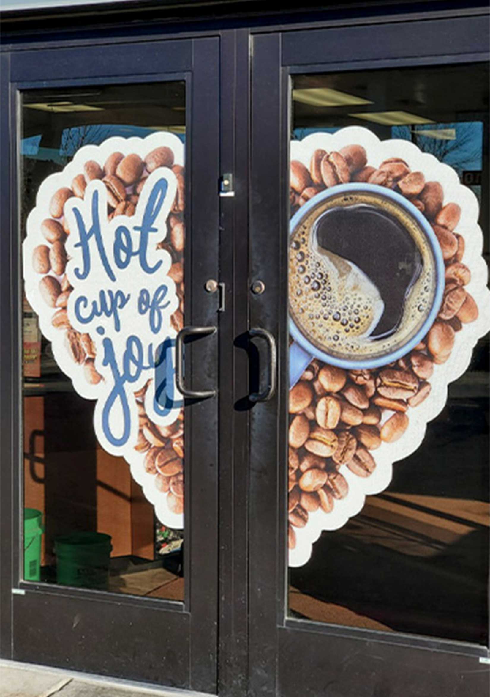 Image of two doors that has large vinyl decals on them that makeup a heart made of coffee beans. One half has a cup of coffee, the other says 'Hot cup of joy'