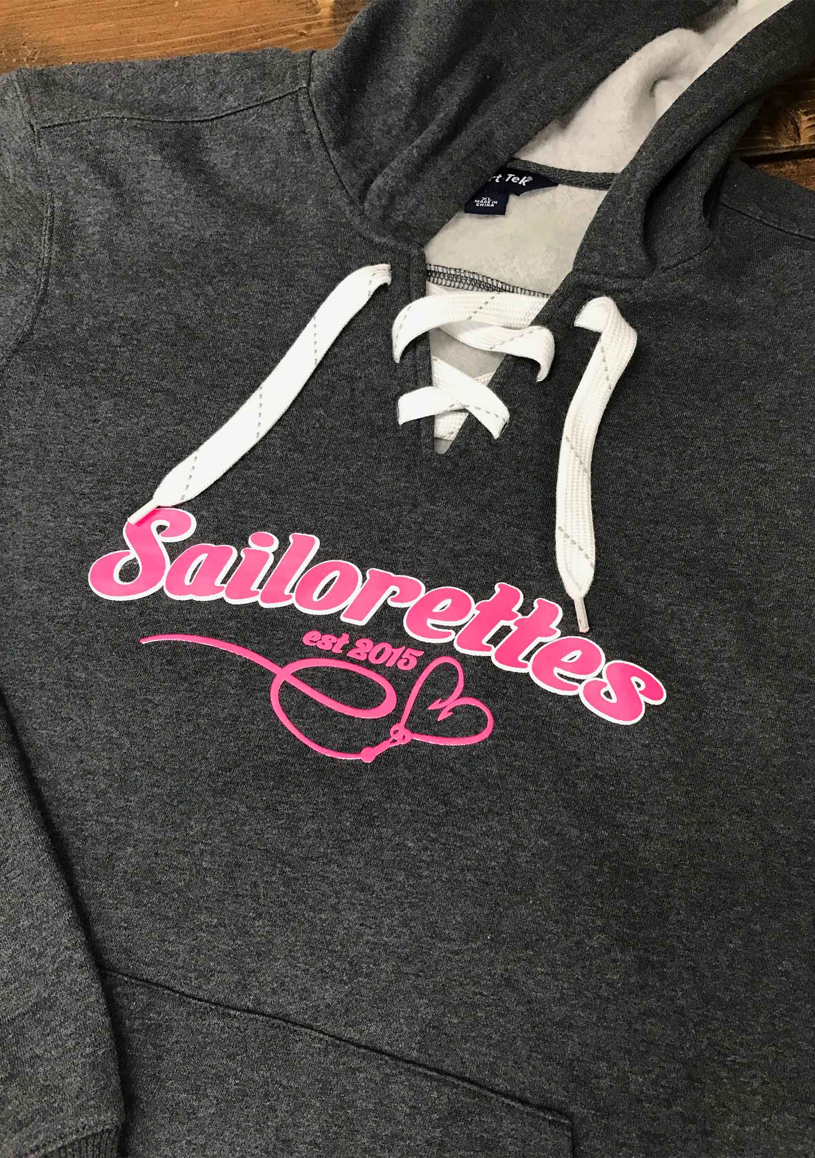 A pink logo for Sailorettes screen printed on the front of a gray hoodie
